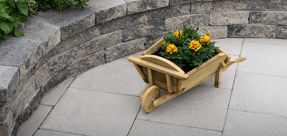 A decorative wooden wheelbarrow planter with yellow flowers sitting on light grey Tobermore patio paving flags.