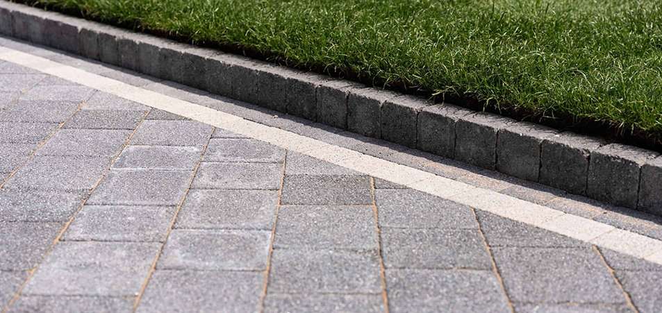 Grey Tobermore block paving driveway featuring a contrasting light border and dark kerb edging next to a green lawn.